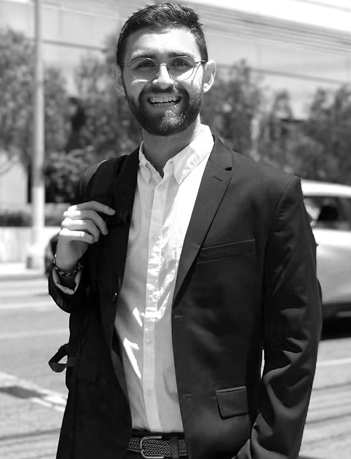 Karl Neumann, smiling, in a dark blazer and white shirt on a city street